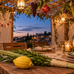 Festlich geschmückte Sukka mit gedecktem Tisch, Früchten, S’chach sowie Etrog und Lulav im warmen Abendlicht.